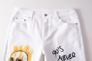 Detail of white denim jeans featuring 90'S NEVER gothic text and yellow flame skull print
