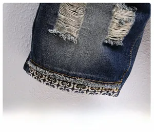 Detail of distressed denim shorts showing ripped holes and branded jacquard tape at the hem