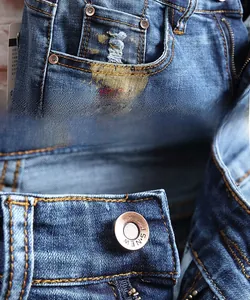 Détail du bouton en cuivre et du rivet sur le short en jean usé avec graffiti coloré