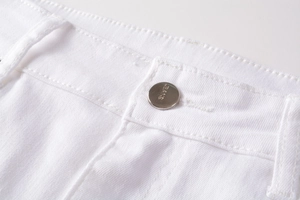 Detailed close-up of white denim jeans featuring engraved silver metal button and fine stitching