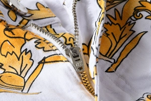 Dettaglio macro della cerniera YKK in metallo argento su pantaloni bianchi barocchi