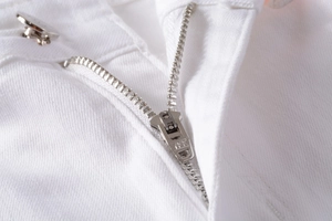 Detailed macro view of white denim fly featuring a premium silver YKK metal zipper