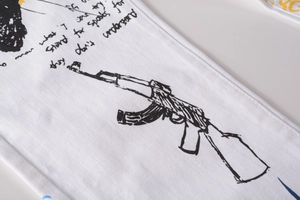 Detail shot of white denim fabric featuring black street art graffiti and AK-47 sketch