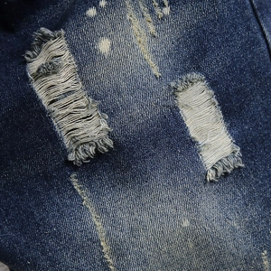 Distressed dark blue denim shorts with ripped holes and white paint splatter details