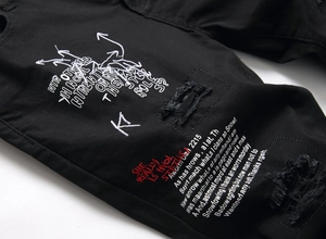 Close-up of black denim shorts with intricate red and white embroidery and distressed details