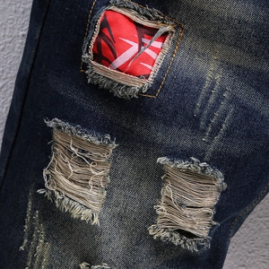 Men's retro distressed denim shorts featuring heavy ripping and red graphic patch detail