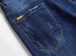 Makroaufnahme einer Herrenjeans-Tasche mit Kontrastnähten und Distressed-Effekt in Blau