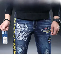 Détail de la broderie tête de tigre et des imprimés jaunes sur jeans bleus pour hommes