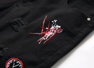 Detail of black denim shorts with clock patch embroidery and distressed ripped texture