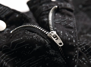 Close-up of high-quality YKK metal zipper on black graffiti patterned denim jeans