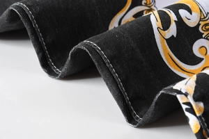 Dettaglio della stampa barocca oro su denim nero con cuciture bianche a contrasto