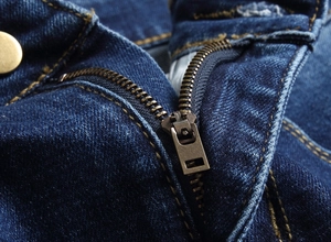 Detailaufnahme des Vintage-Bronze-Reißverschlusses und der orangefarbenen Naht der Jeans