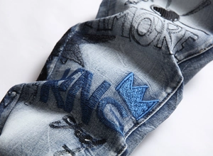 Macro detail of crown embroidery and graphic print on light blue wash denim jeans
