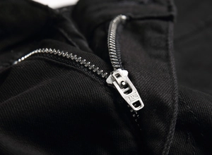 Macro shot of silver metal zipper with JEANS engraving on black denim fabric