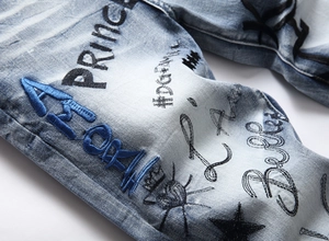 Detail of blue stretch denim jeans featuring heavy embroidery and street graffiti prints