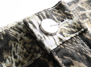 Macro detail of jeans silver metal button with engraved text on snake pattern fabric