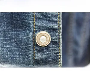 Detailed close-up of metal jeans buttons and double-row stitching on blue denim jacket