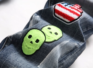 Detail of blue washed denim jeans with neon green skull and American flag patches