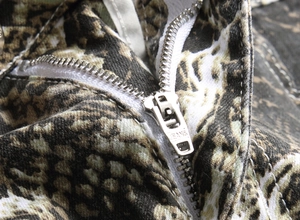 Macro detail of high-quality silver metal zipper with JEANS engraving on snakeskin pants