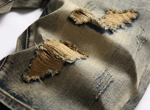 Close-up of distressed vintage denim with washed cat whiskers and heavy ripped details
