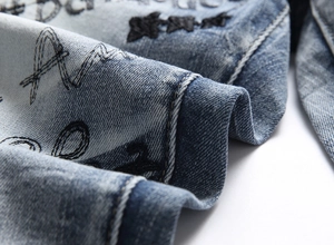 Detail of heavy embroidery and graffiti print on blue washed denim fabric