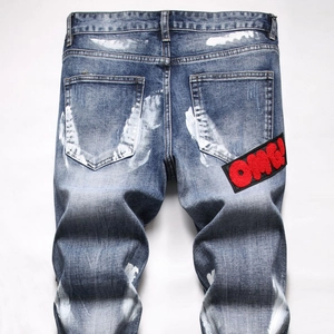 Detail view of denim jeans featuring white paint splatter and red OMG chenille patch