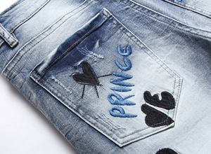 Detail of blue washed denim jeans showing heavy embroidery on back pocket with Prince text