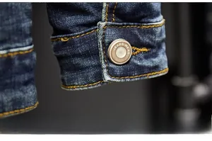 Detail of dark blue denim jacket cuff with yellow stitching and vintage metal button
