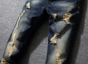 Detailed close-up of vintage distressed denim pants with rip details and faded wash