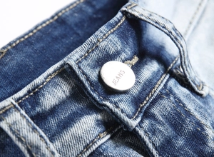 Detailed macro view of the silver metal button and golden stitching on blue denim jeans