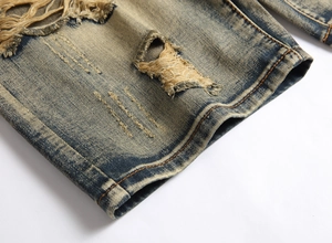 Detail of distressed blue denim fabric with heavy wash, ripped holes, and retro texture