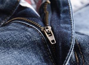 Detailed macro shot of vintage brass zipper and reinforced stitching on dark blue denim pants