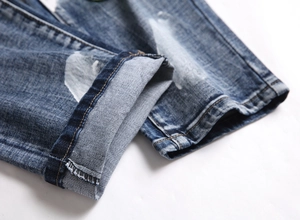 Detailed close-up of dark blue washed denim jeans with white paint spray and cuffed hem
