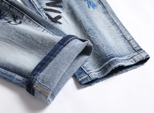 Close-up of light wash denim hem featuring KIM typography and blue lightning embroidery