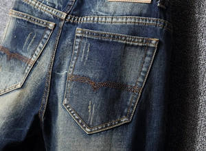 Close-up of vintage distressed denim back pocket with orange double stitching details