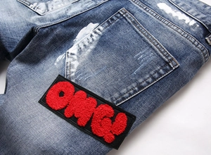 Detail of blue jeans featuring white paint splatter and red OMG! chenille embroidery patch