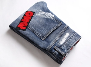 Macro detail of red fuzzy letter patch and white paint splatter on blue washed jeans