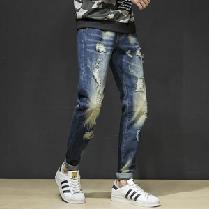 Detailed view of men's slim fit blue jeans with heavy distressed ripped effects and whiskered wash
