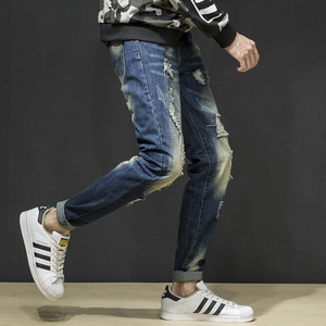 Detail of distressed blue men's slim jeans with vintage ripped effects and raw edge hems