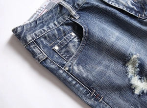 Close-up of distressed denim pocket with silver rivets and vintage washed fabric texture