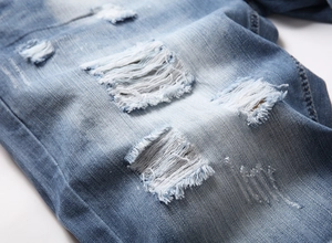 Macro shot of light blue denim shorts showing heavy distressed texture and ripped detail