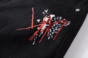 Détail de la broderie graffiti multicolore et du rivet argenté sur un jean noir