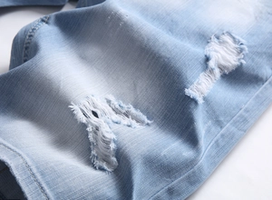 Detailed macro view of distressed light blue denim shorts with ripped knee and frayed texture