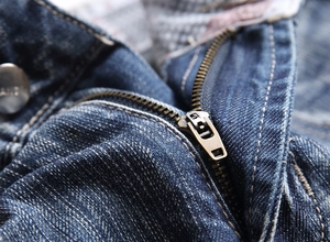 Close-up of bronze metal zipper and engraved button on washed denim shorts