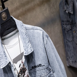 Detail of light blue denim jacket with RUN HARD embroidery and metal button accents