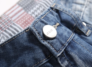 Macro shot of blue denim shorts waist showing metal button and orange stitching
