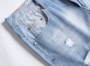 Detailed view of light blue washed denim with distressed holes and yellow stitching