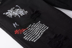 Détails de jean noir avec déchirures artisanales, imprimés graffiti et broderies rouges