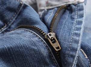 Detailed close-up of antique bronze metal zipper and indigo denim stitching on shorts