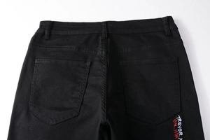Détail du jean noir extensible montrant la taille et la broderie TREVOR ON HIM sur la poche